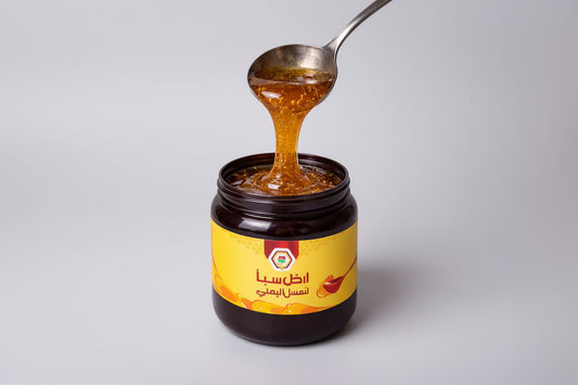 Jar of honey with a spoon lifting some honey, on a light gray background