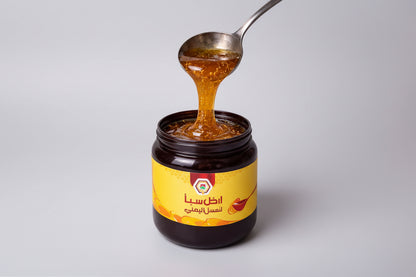 Jar of honey with a spoon lifting some honey, on a light gray background